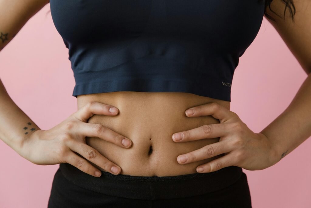 A close-up shot of a woman's toned stomach with hands on hips, against a pink background.